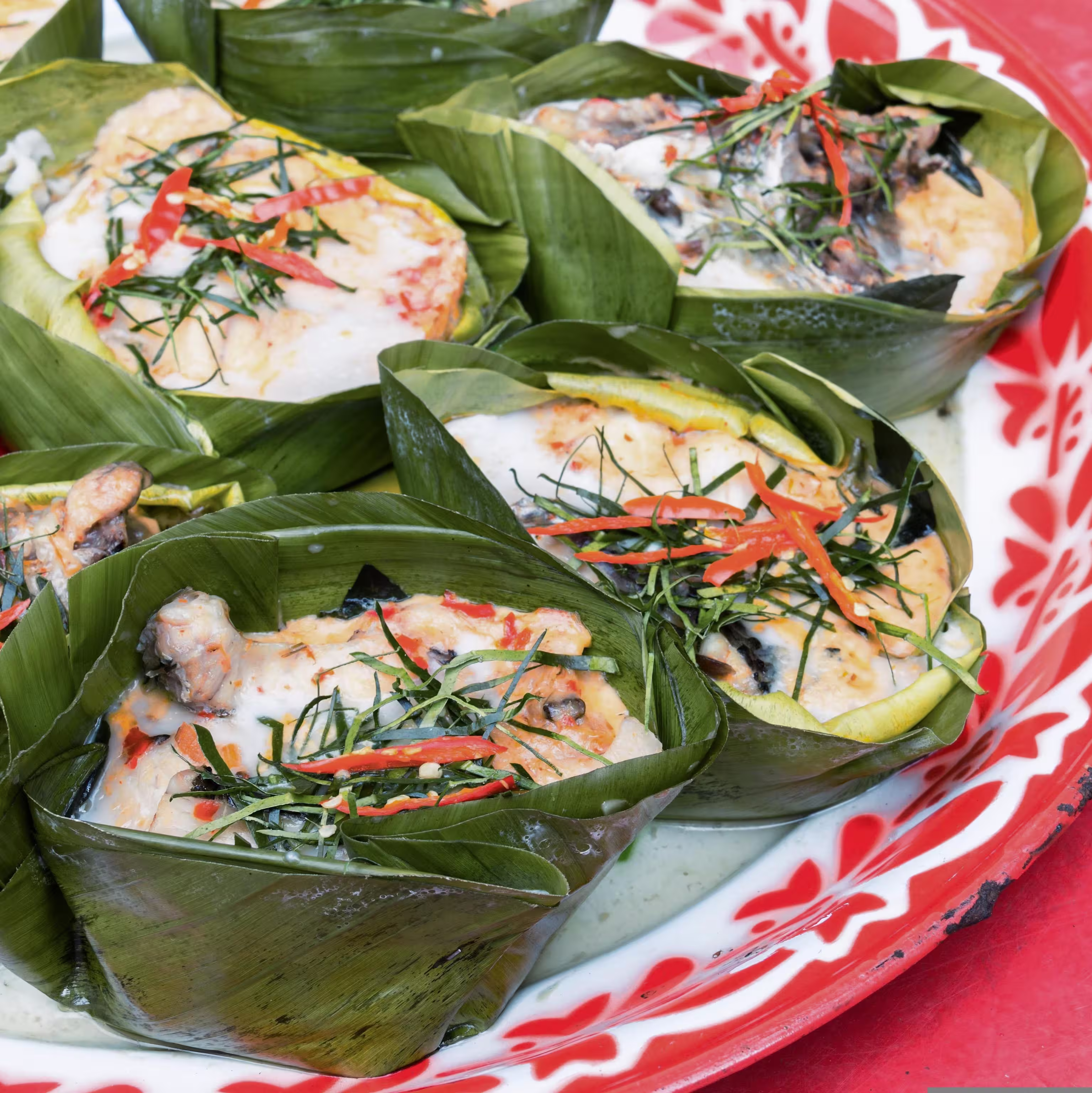 Curry leaves wrapped around food in a white plate with a pink edge.