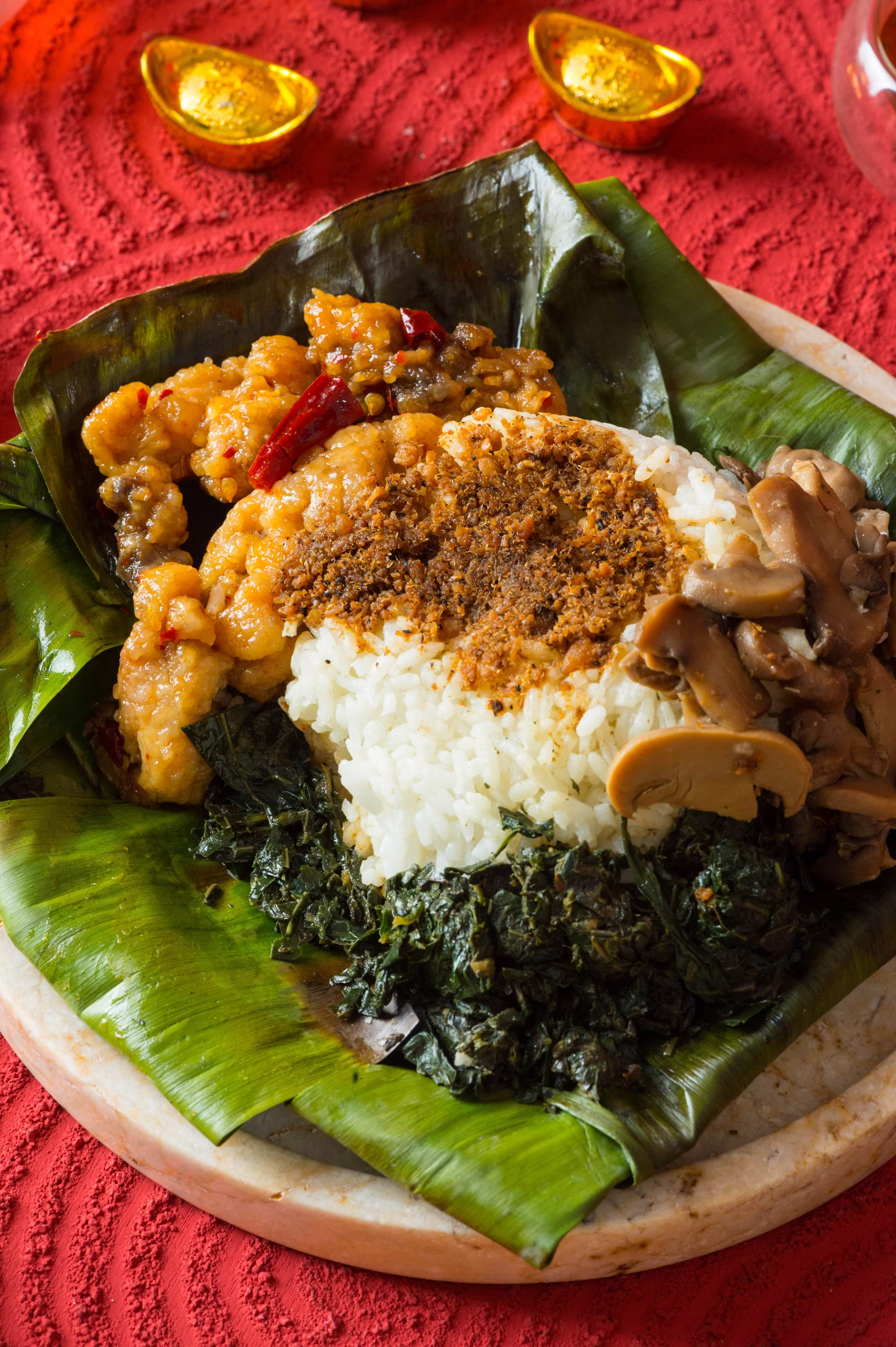Plated on a granite plate is a huge leaf with tempered curry leaves rice and nuts and side dishes to eat alongside with the rice.